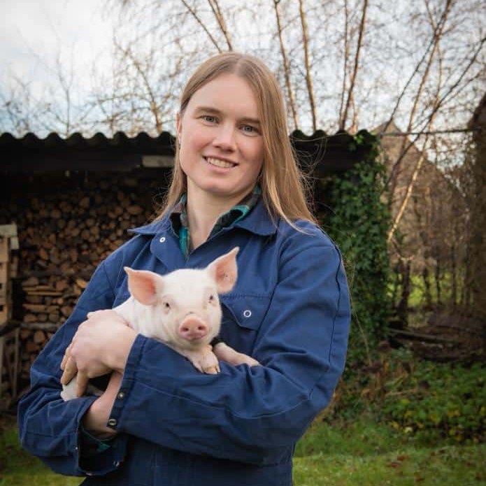 Eveline met een biggetje op haar hoeve in Damme